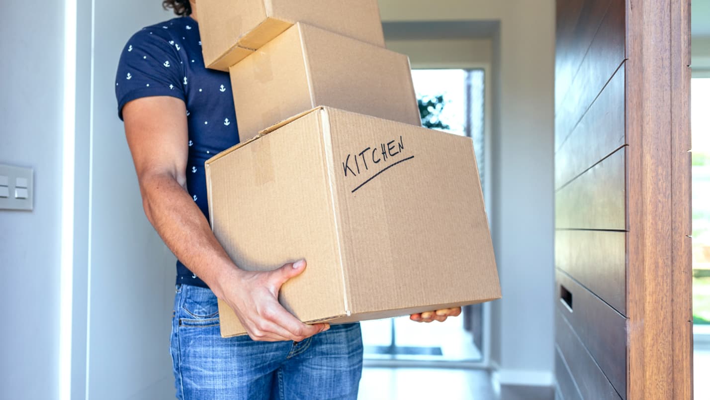A man carries a stack of boxes, one is marked with the word “kitchen”.