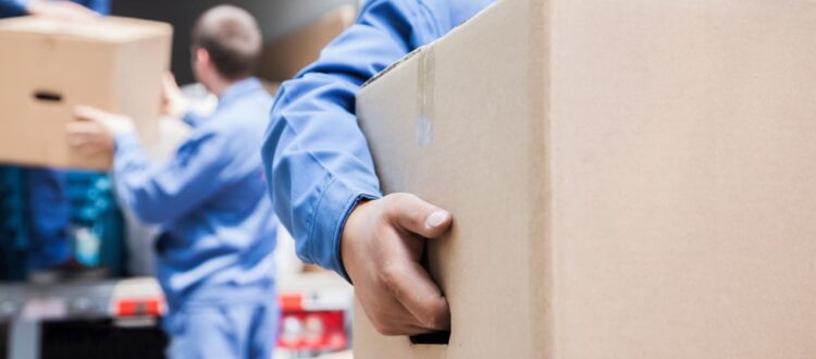 Men in blue jumpsuits carry boxes to a large moving truck.